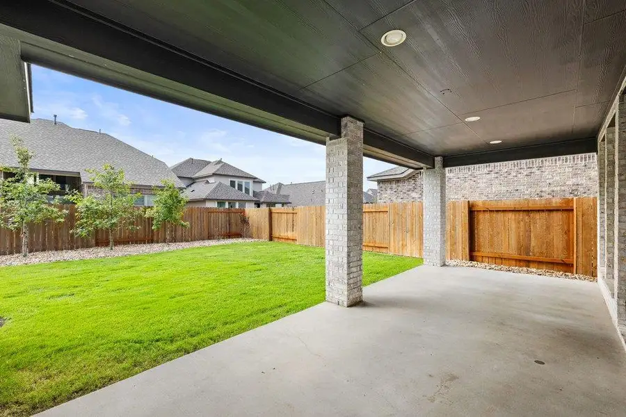 A spacious covered patio provides a delightful outdoor living space overlooking a vibrant green lawn.