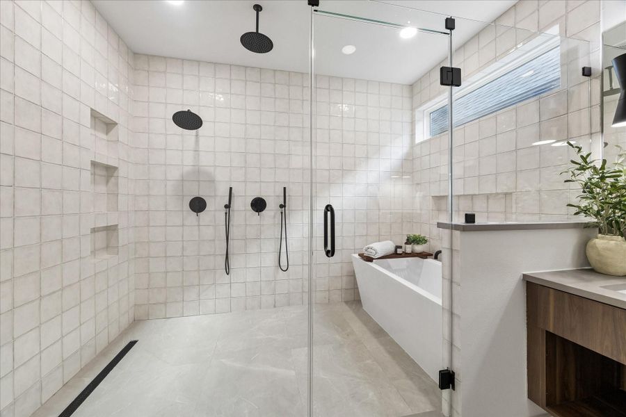 An oversized walk through shower featuring dual rainfall heads, seamless glass, and full height tile creates a resort inspired experience every day.