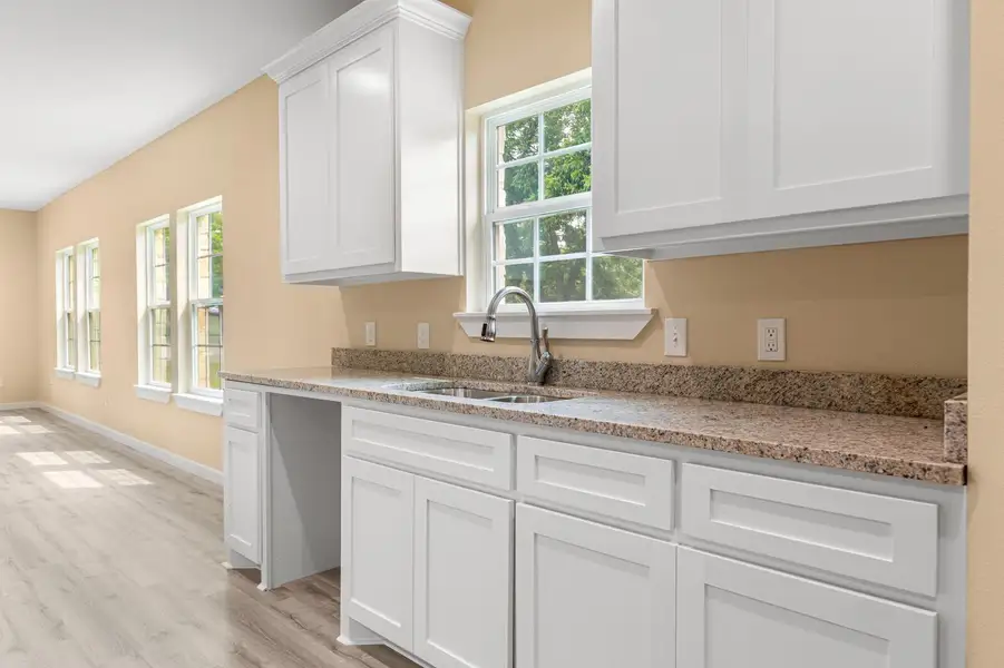Kitchen featuring light wood-style floors, white cabinets, and light stone counters