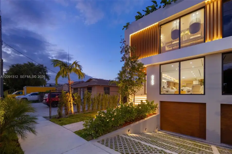Contemporary multi-story exterior featuring floor-to-ceiling glass windows, integrated accent lighting, wood-slat architectural detailing, and a multi-car subterranean-level garage with a concrete paver driveway Contemporary multi-story exterior featuring floor-to-ceiling glass windows, integrated accent lighting, wood-slat architectural detailing, and a multi-car subterranean-level garage with a concrete paver driveway