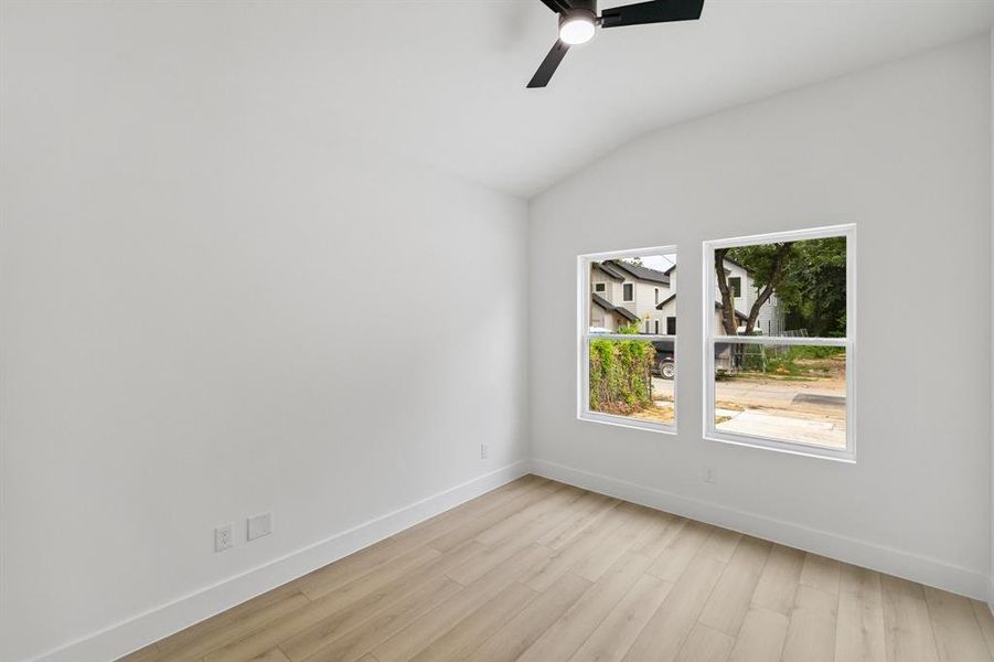 Empty room featuring vaulted ceiling, light wood finished floors, and a ceiling fan