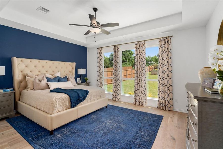 Bedroom with ceiling fan, a raised ceiling, light hardwood / wood-style flooring, and multiple windows