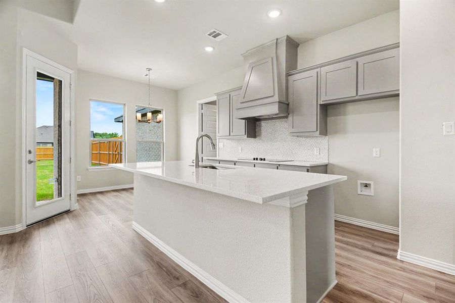Spacious kitchen featuring a large island with a composite countertop, wood-finish flooring, recessed lighting, and a white tile backsplash Spacious kitchen featuring a large island with a composite countertop, wood-finish flooring, recessed lighting, and a white tile backsplash