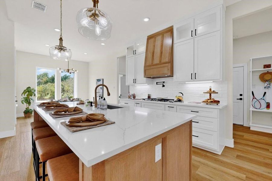 Kitchen with decorative light fixtures, tasteful backsplash, white cabinetry, light wood-type flooring, and light brown cabinetry Kitchen with decorative light fixtures, tasteful backsplash, white cabinetry, light wood-type flooring, and light brown cabinetry
