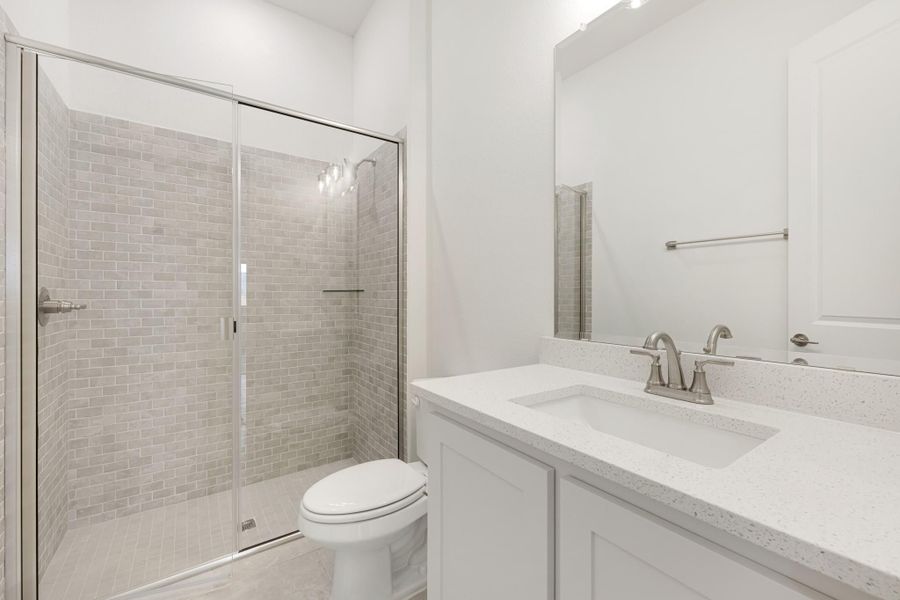Bathroom with glass-enclosed tile shower, white vanity with quartz countertop, and toilet Bathroom with glass-enclosed tile shower, white vanity with quartz countertop, and toilet