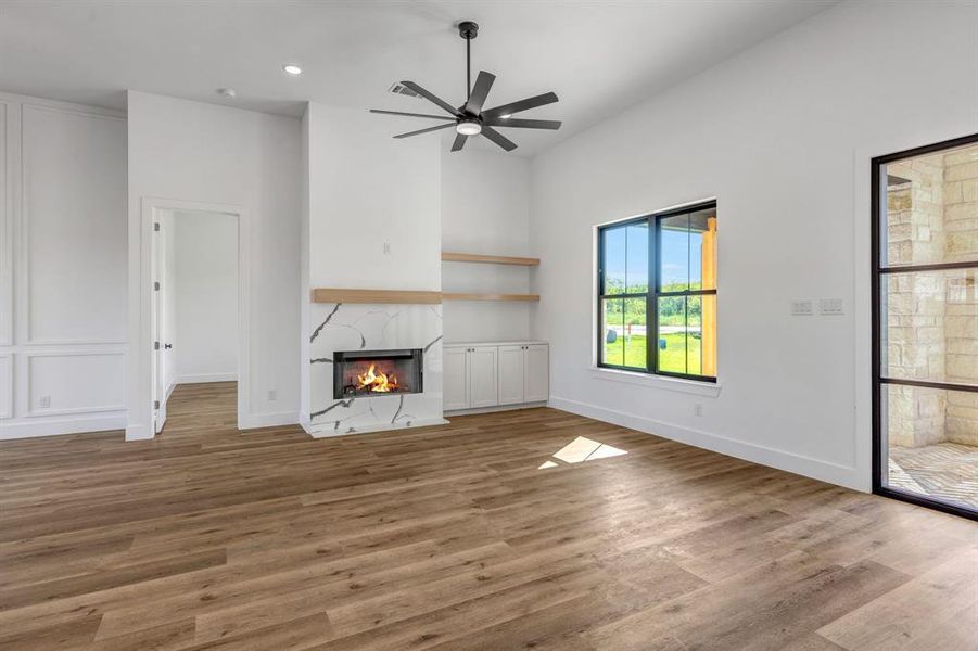Living room with a warm lit fireplace, light wood-style floors, recessed lighting, and ceiling fan