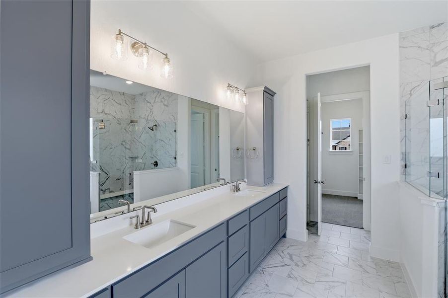Bathroom featuring light marble finish flooring, double vanity, and a marble finish shower
