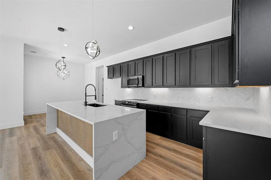 Kitchen featuring backsplash, sink, light stone counters, light hardwood / wood-style floors, and stainless steel appliances