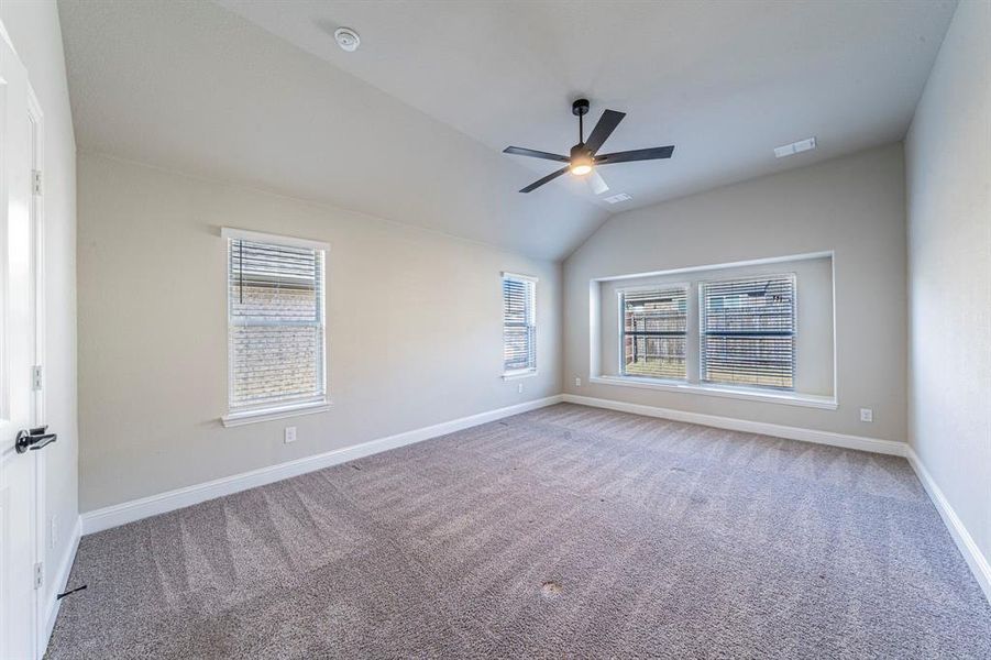 Spacious room featuring vaulted ceilings, a contemporary ceiling fan with integrated lighting, and carpeted flooring