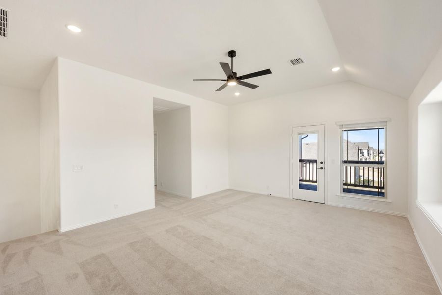 Empty bedroom with vaulted ceiling, ceiling fan, carpet flooring, and glass door leading to balcony