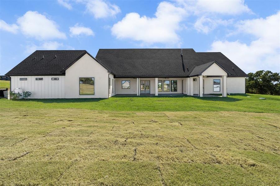 View of front facade with a front yard, a patio, a shingled roof, and stucco siding View of front facade with a front yard, a patio, a shingled roof, and stucco siding