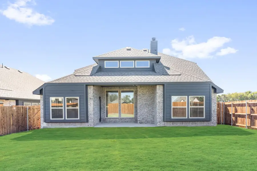 Rear exterior of single-story brick home with gray siding, large windows, patio, and fenced backyard with green lawn Rear exterior of single-story brick home with gray siding, large windows, patio, and fenced backyard with green lawn