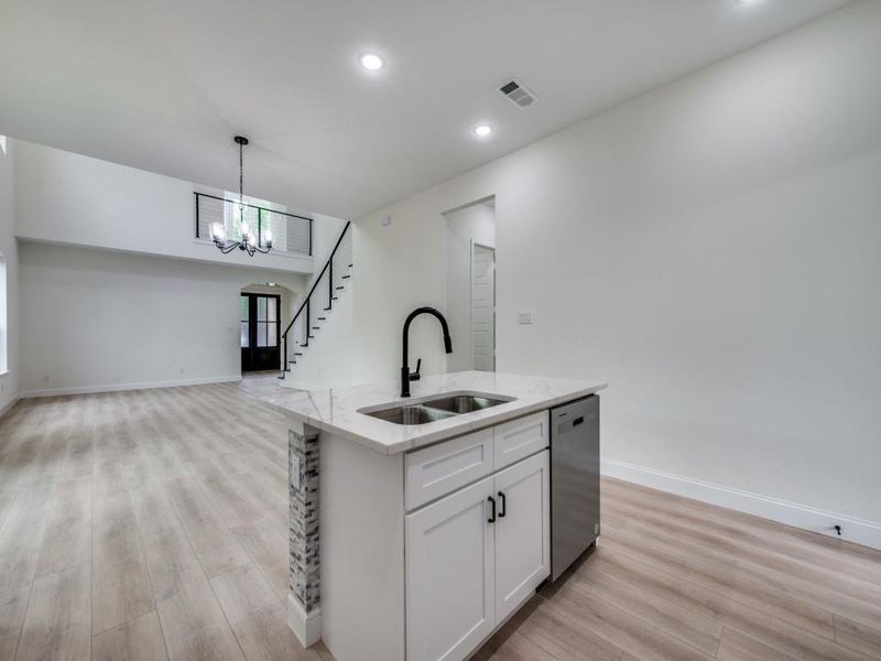 Kitchen with a sink, dishwasher, light wood-style floors, open floor plan, and light stone counters