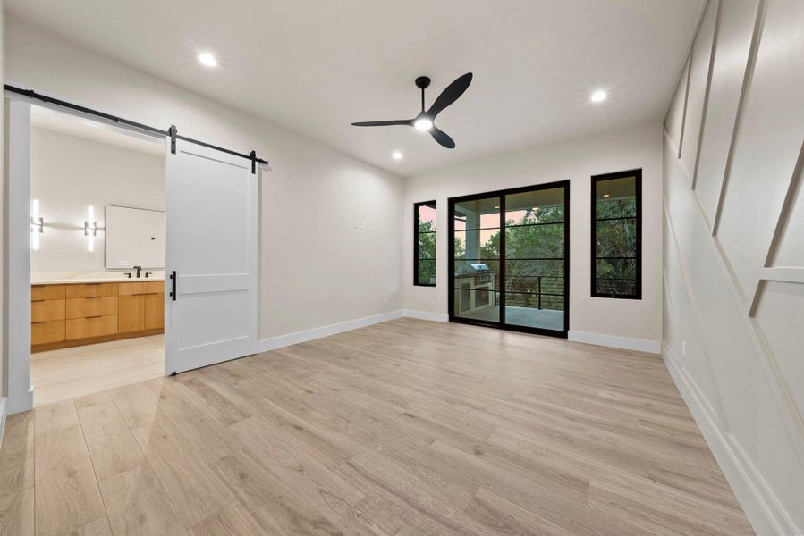 A well-lit room with light wood flooring, an outdoor grilling area, and a stylish barn door leading to an adjoining bathroom.