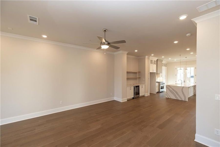 Unfurnished living room with crown molding, dark wood finished floors, a ceiling fan, recessed lighting, and beverage cooler