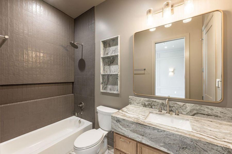 Moody hues and warm metallic accents give this bath a refined, designer-forward feel. A statement round mirror, tailored vanity, and tiled tub surround come together to create a space that feels elevated yet effortlessly functional.
