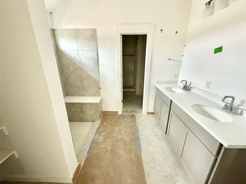 Bathroom featuring double vanity, light tile patterned floors, and tiled shower