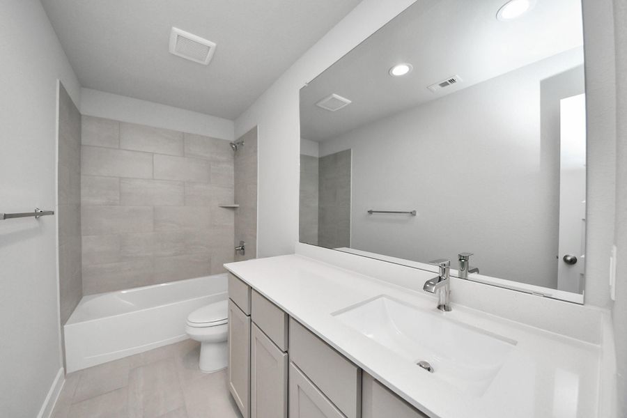 Secondary bath features tile flooring, bath/shower combo with tile surround, light stained wood cabinets, beautiful light countertop. Sample photo of completed home with similar floor plan. Actual colors and selections may vary.