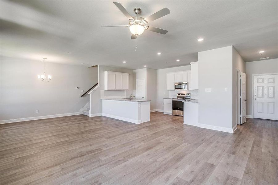 Unfurnished living room featuring ceiling fan, light wood-type flooring, and a chandelier