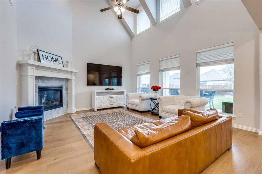 Living room featuring a towering ceiling, light wood-type flooring, ceiling fan, and a tiled fireplace