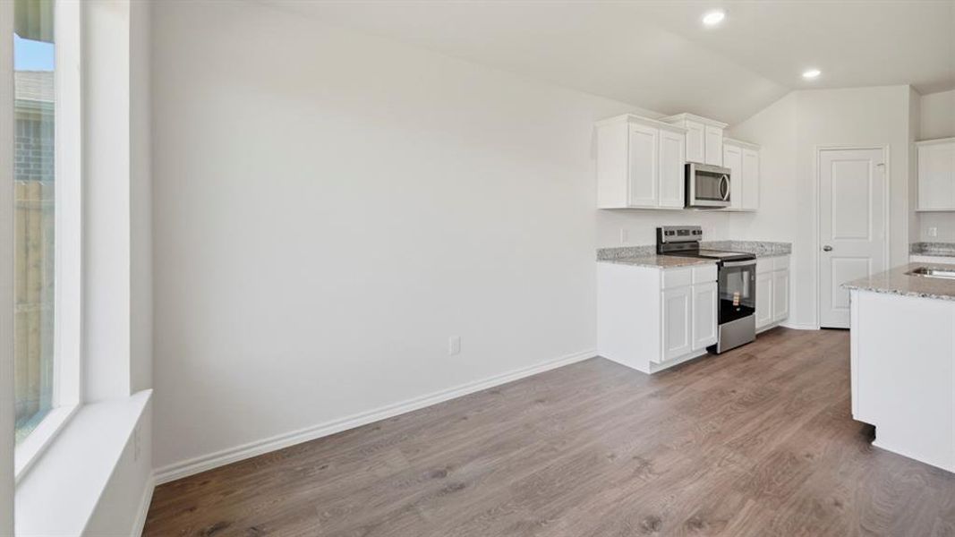 Kitchen featuring white cabinetry, light stone countertops, stainless steel appliances, dark wood-style flooring, and lofted ceiling