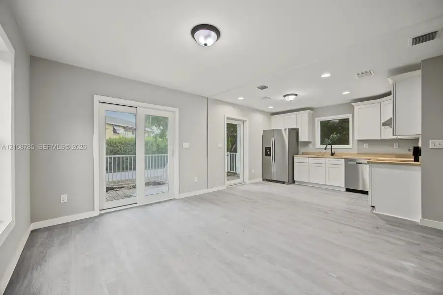 Open-concept space featuring wood-finish flooring, white shaker cabinetry, stainless steel appliances, neutral wall color, and glass sliding door access Open-concept space featuring wood-finish flooring, white shaker cabinetry, stainless steel appliances, neutral wall color, and glass sliding door access