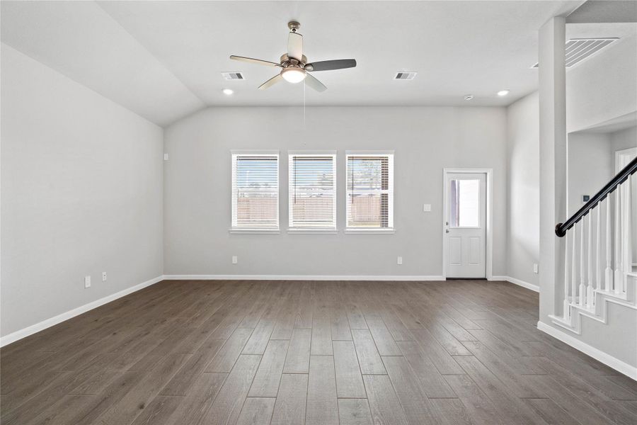A bright and airy open-concept space featuring wood-look tile flooring, sloped ceilings with recessed lighting and ceiling fan, and abundant natural light from large windows (fitted with blinds). An access door to the back covered patio is conveniently located for ease of indoor to outdoor living.