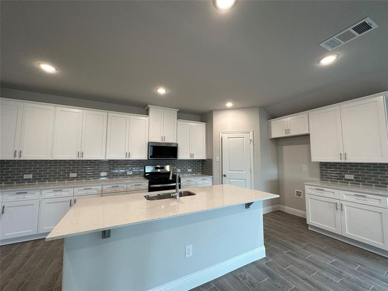 Kitchen with a kitchen island with sink, appliances with stainless steel finishes, dark hardwood / wood-style floors, and white cabinetry