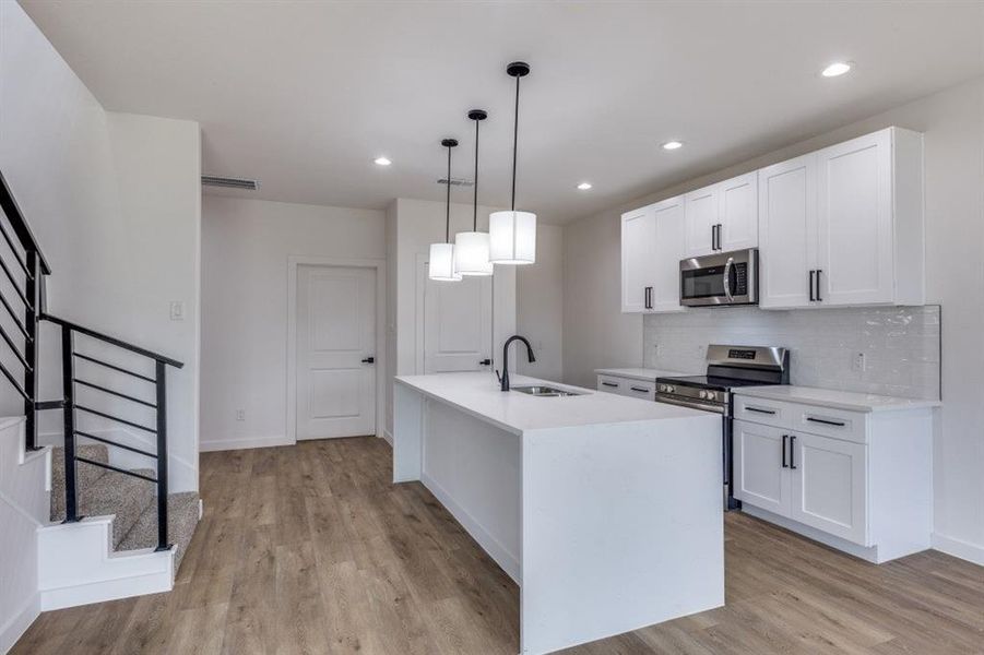 Kitchen featuring stainless steel appliances, decorative backsplash, pendant lighting, white cabinets, and light stone counters Kitchen featuring stainless steel appliances, decorative backsplash, pendant lighting, white cabinets, and light stone counters
