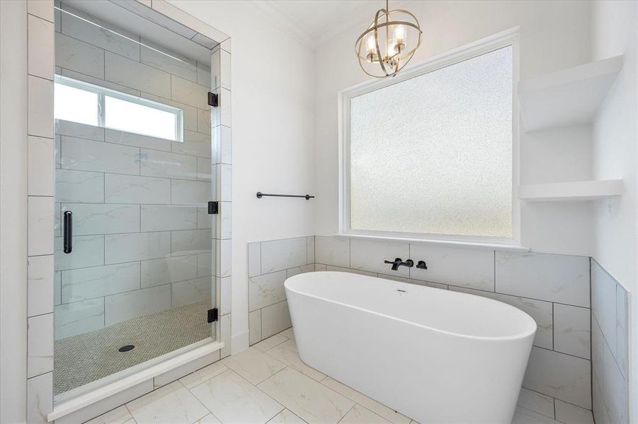 Primary Bathroom with marble look tile flooring, a freestanding tub, a stall shower, tile walls, and a chandelier Primary Bathroom with marble look tile flooring, a freestanding tub, a stall shower, tile walls, and a chandelier
