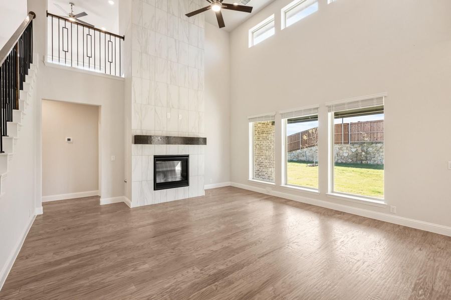 Open living room with two-story ceiling, floor-to-ceiling tile fireplace, hardwood floors, and large windows Open living room with two-story ceiling, floor-to-ceiling tile fireplace, hardwood floors, and large windows