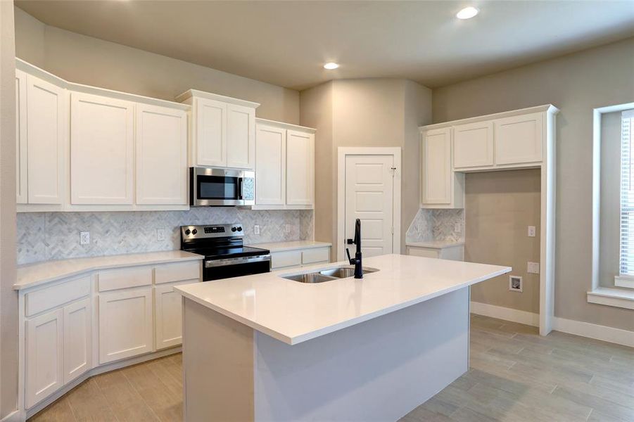 Kitchen featuring backsplash, stainless steel appliances, white cabinetry, an island with sink, and light wood-style flooring Kitchen featuring backsplash, stainless steel appliances, white cabinetry, an island with sink, and light wood-style flooring