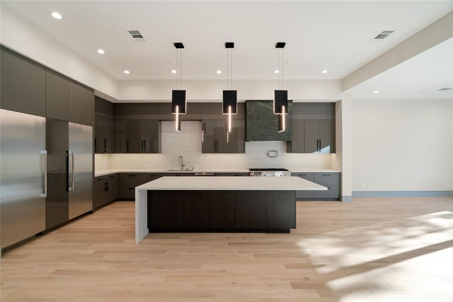 This photo showcases a modern kitchen with sleek cabinetry, a large central island, and contemporary pendant lighting. It features stainless steel appliances and light wood flooring, creating a spacious and elegant atmosphere.