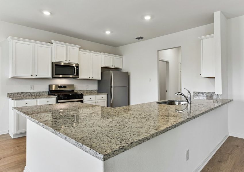 Kitchen featuring a granite peninsula, white cabinetry, a stainless refrigerator, and a microwave.