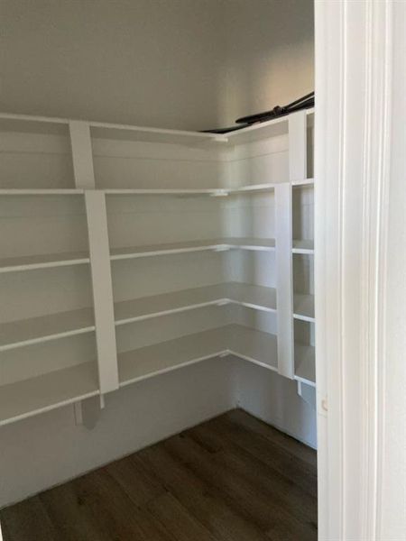 Corner pantry featuring multiple white built-in shelves and wood-finish flooring