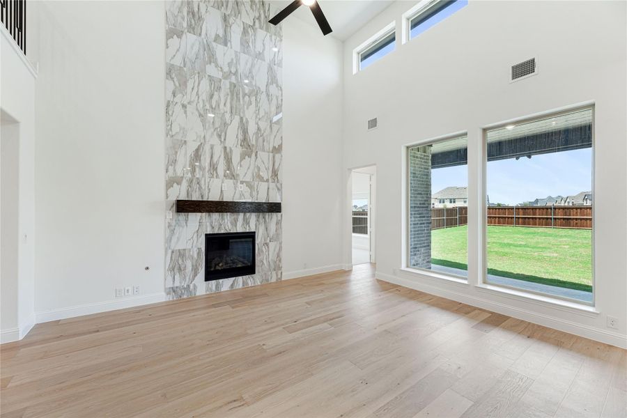 Open living room with two-story marble tile fireplace, hardwood floors, and large windows overlooking backyard