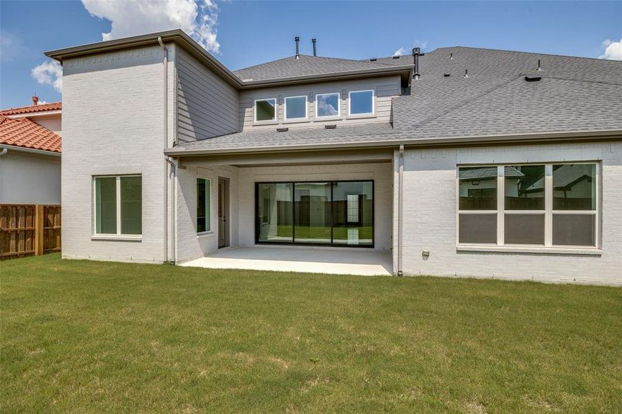 Expansive backyard featuring a manicured lawn, covered patio, and large sliding glass doors Expansive backyard featuring a manicured lawn, covered patio, and large sliding glass doors