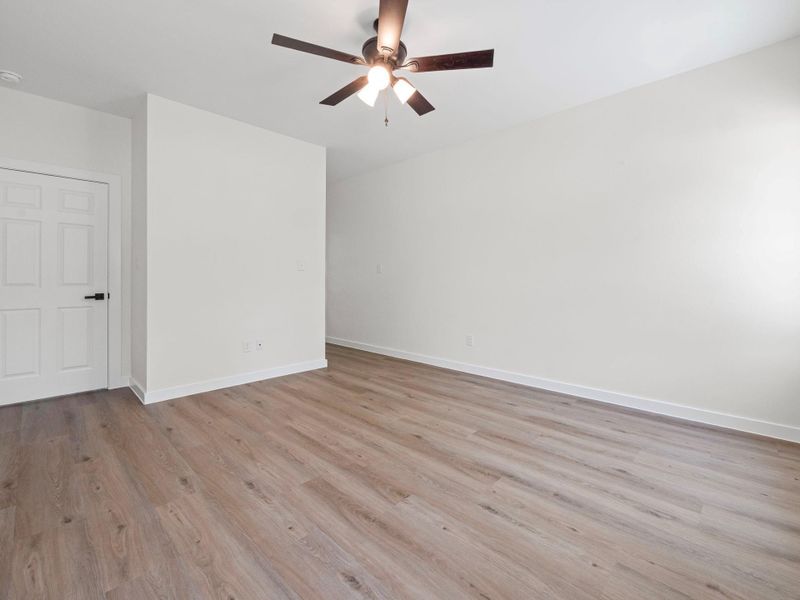 Spacious room with wood-finish flooring, white walls, and a ceiling fan with integrated lighting