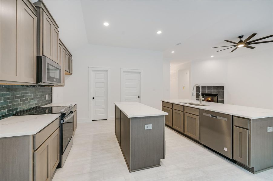 Kitchen with tasteful backsplash, a kitchen island, appliances with stainless steel finishes, a fireplace, and a sink