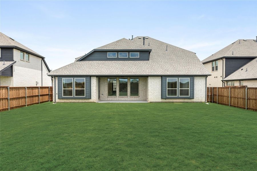 Rear exterior of brick home with gray trim, large windows, patio doors, and fenced backyard with green lawn