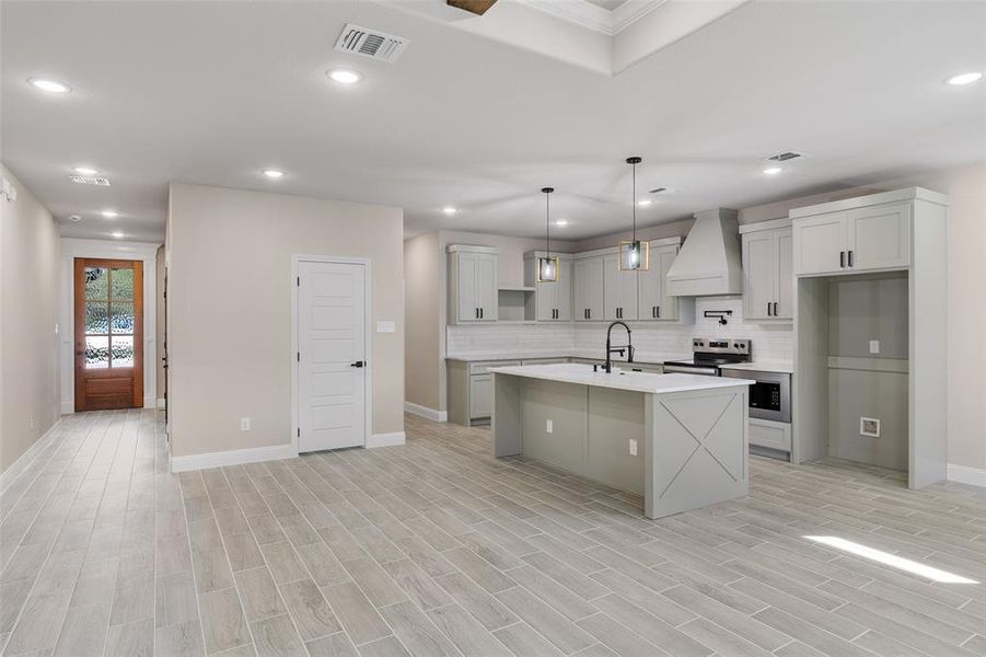 Kitchen featuring hanging light fixtures, tasteful backsplash, a kitchen island with sink, custom exhaust hood, and appliances with stainless steel finishes