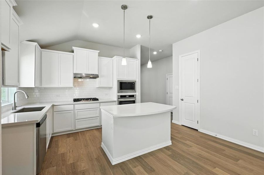 Kitchen with appliances with stainless steel finishes, under cabinet range hood, dark wood-style flooring, decorative backsplash, and vaulted ceiling Kitchen with appliances with stainless steel finishes, under cabinet range hood, dark wood-style flooring, decorative backsplash, and vaulted ceiling