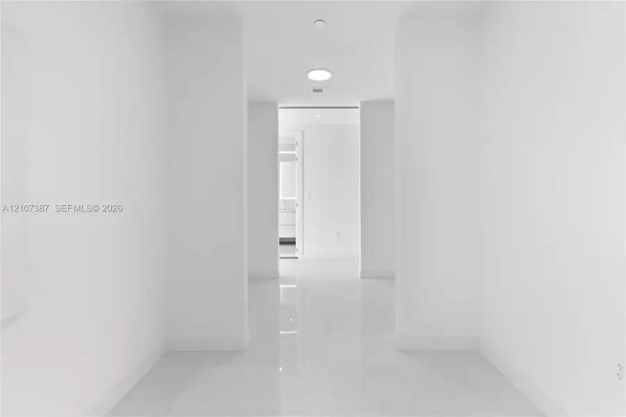 Interior corridor featuring polished stone-finish tile flooring, clean white walls, and recessed ceiling lighting