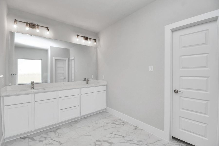 Escape to a spa-like oasis in this primary bathroom. Enjoy a walk-in shower with tile surround, a separate garden tub with custom detailing, and an elegant vanity featuring light countertops, modern hardware, and beautiful vanity lights. Experience luxury and relaxation in every detail. Sample photo of completed home with similar floor plan. Actual colors and selections may vary.