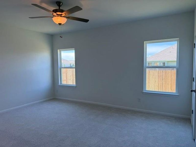 Carpeted room with a ceiling fan light fixture, two double-hung windows, and painted walls Carpeted room with a ceiling fan light fixture, two double-hung windows, and painted walls