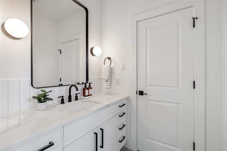 Secondary bathroom featuring a quartz countertop, modern black fixtures, a sleek black-framed mirror, and stylish lighting for a contemporary and polished look.