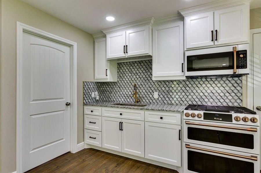 Kitchen with high end stove, light stone counters, dark wood-type flooring, white cabinetry, and backsplash