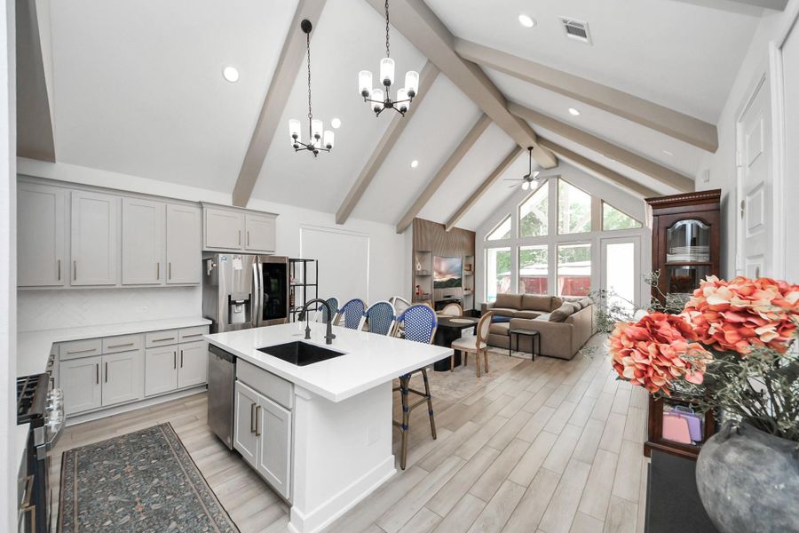 This photo showcases a bright, open-concept kitchen and living area with vaulted ceilings and exposed beams. The kitchen features modern cabinetry, a large island with a sink, and stainless steel appliances. The living area has large windows providing plenty of natural light and a cozy seating arrangement. This photo showcases a bright, open-concept kitchen and living area with vaulted ceilings and exposed beams. The kitchen features modern cabinetry, a large island with a sink, and stainless steel appliances. The living area has large windows providing plenty of natural light and a cozy seating arrangement.