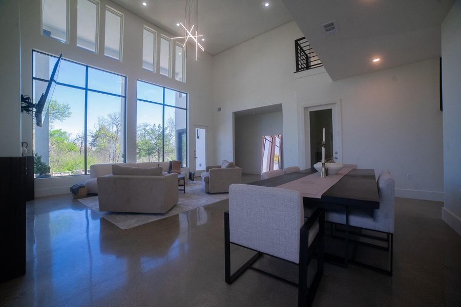 This spacious living area features high ceilings, large windows with scenic views, and an open layout. The modern lighting and sleek finishes enhance the contemporary design, while the dining and seating areas offer ample space for entertaining.