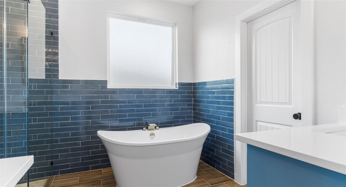 Bathroom featuring tile walls, a freestanding tub, wood tiled floors, vanity, and a wainscoted wall